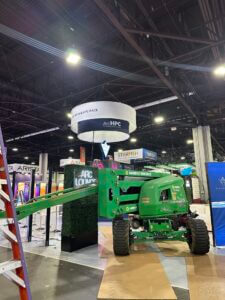 A forklift is positioned to set up the ARC Compute rental trade show booth in a busy exhibition hall.