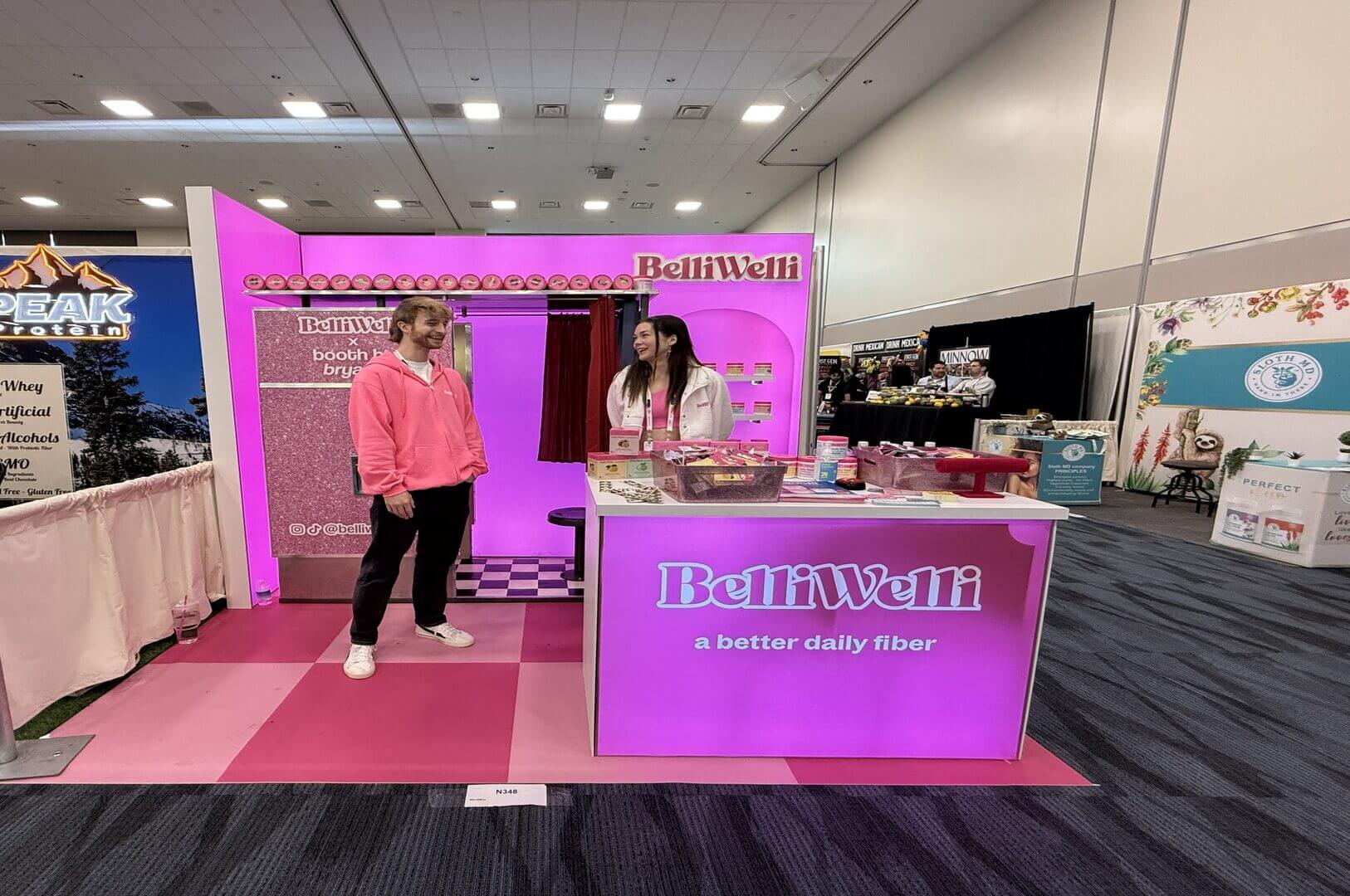 BelliWelli's 10x10 rental booth with a checkered floor and Booth by Bryant photo booth at Natural Products Expo West 2025.