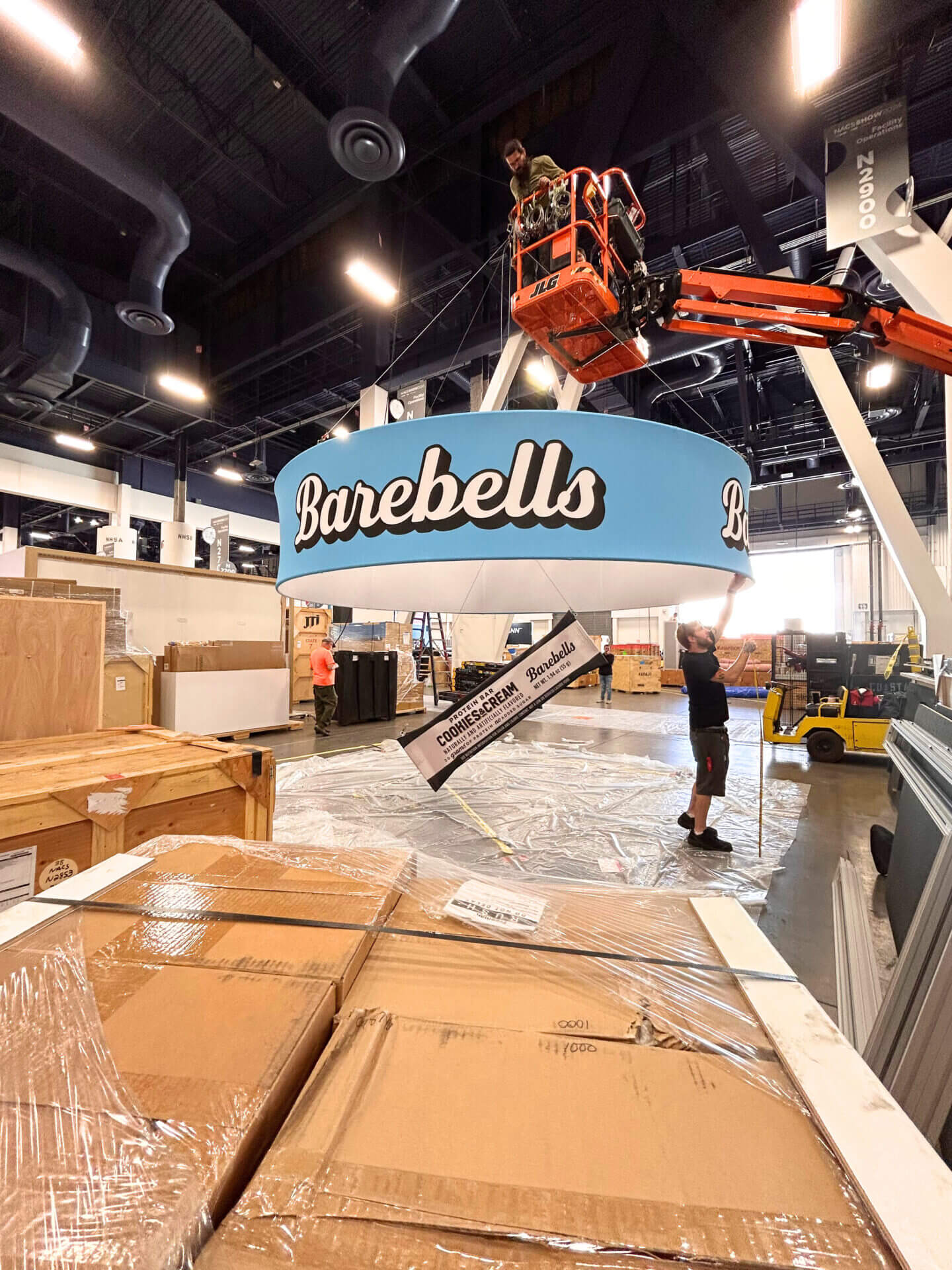 Barebells circular sign being hung by a forklift with a protein bar in the middle.